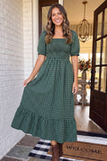 Woman wearing The Everly Plaid Dress, forest green plaid smocked maxi, in a doorway