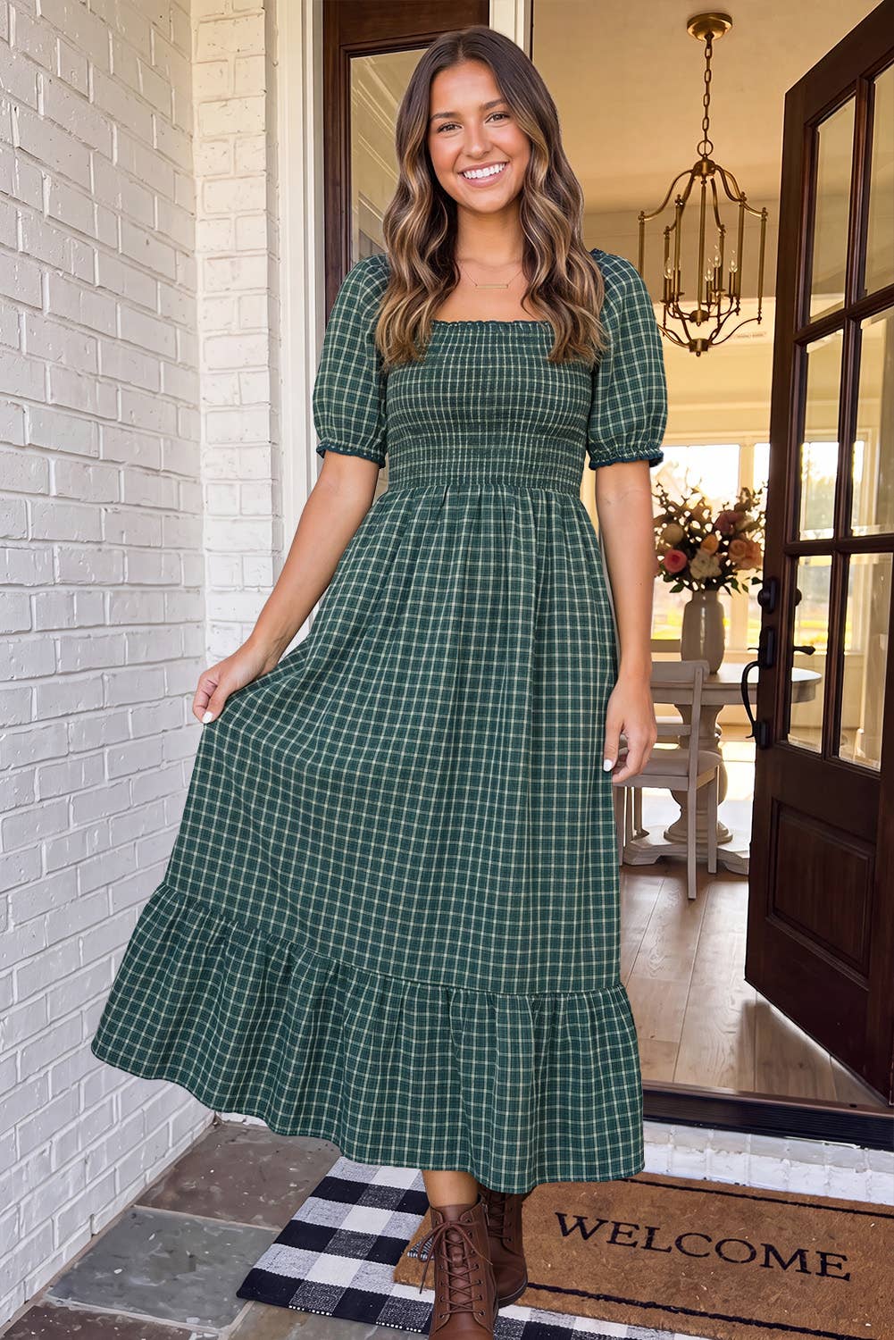 Woman wearing The Everly Plaid Dress, forest green plaid smocked maxi, in a doorway