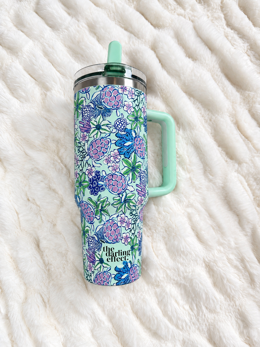 The Coastal Cove Tumbler, a seafoam 40 oz tumbler with sea turtles, coral and flowers and a mint flip straw
