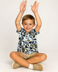 Boy sitting with arms up, wearing The Castaway Camo Polo in blue and green fish camo