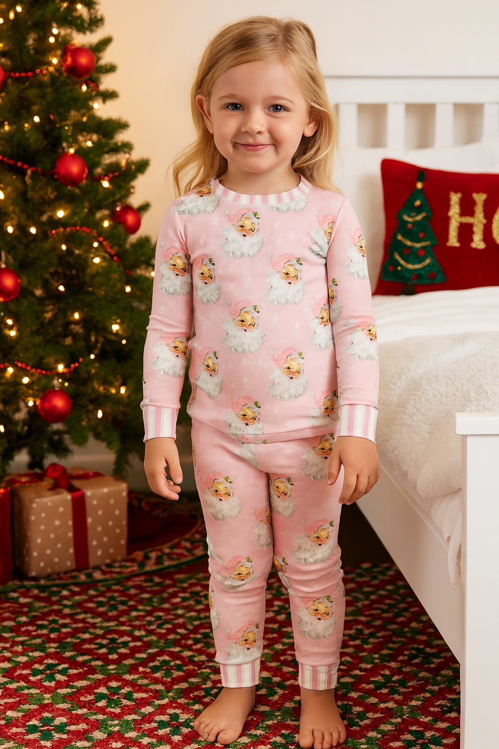 Girl wearing the pink Santa Baby Pajama Set in front of a Christmas tree