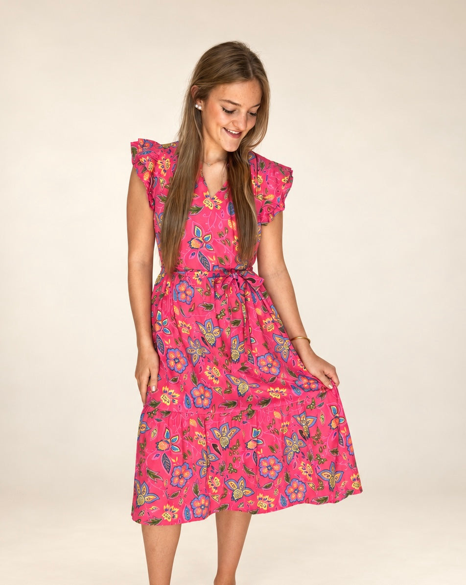 Woman wearing The Posie Dress, pink floral midi with flutter sleeves, holding the skirt