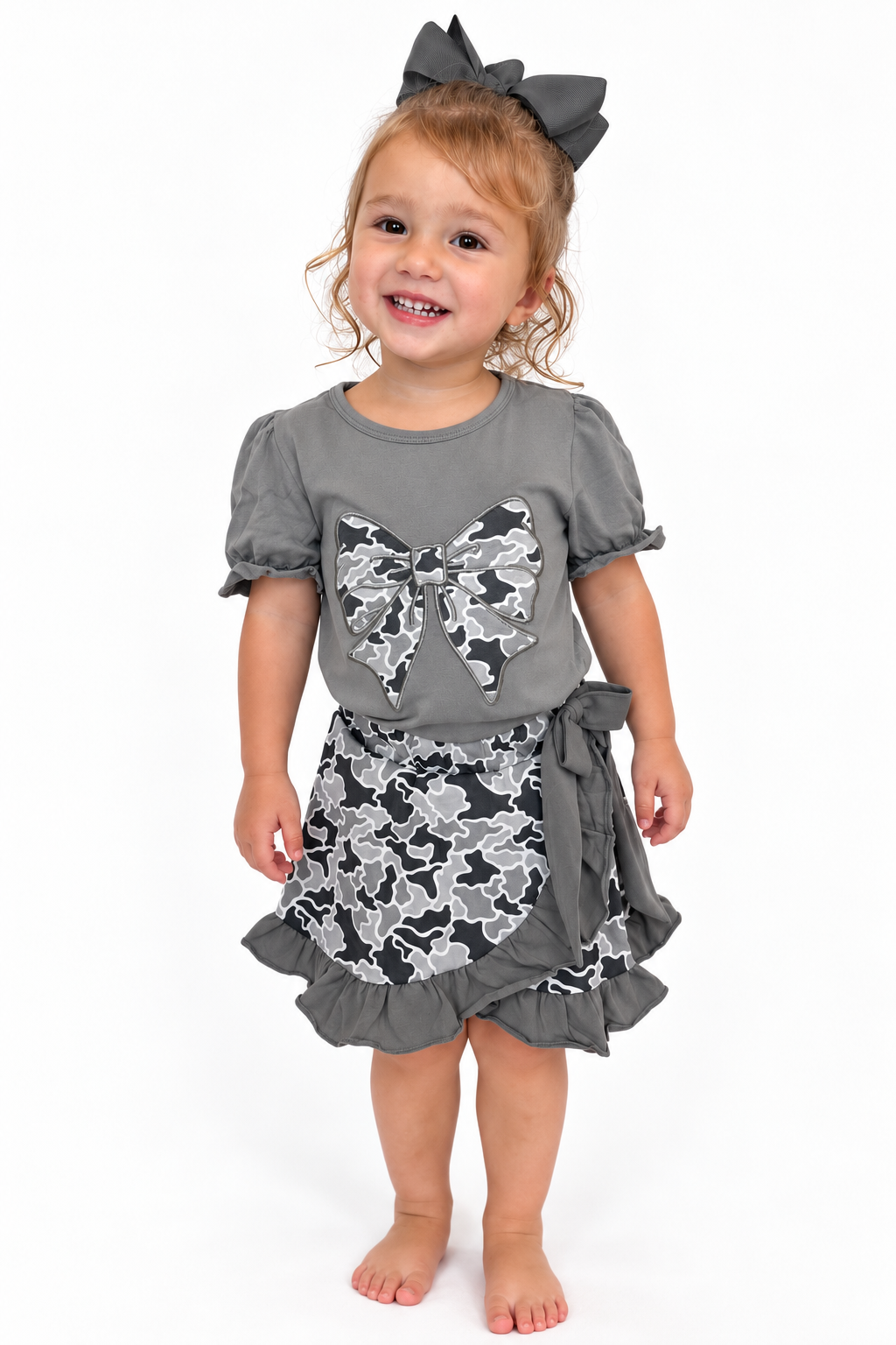 Girl wearing The Collins Camo Bow Skort Set, charcoal top with camo bow and ruffle camo skort
