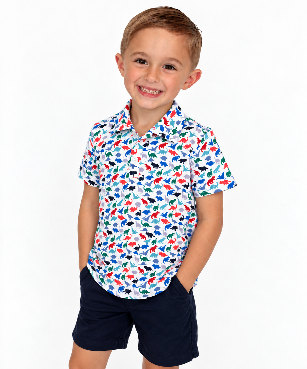 Boy wearing The Little Roar Polo, white polo with colorful dinosaur print, with navy shorts