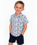 Boy wearing The Little Roar Polo, white polo with colorful dinosaur print, with navy shorts