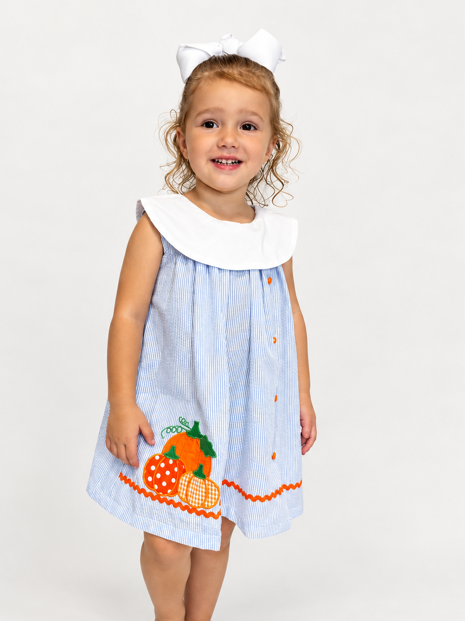 Girl wearing The Pumpkin Patch Dress, blue seersucker with white collar and pumpkin applique