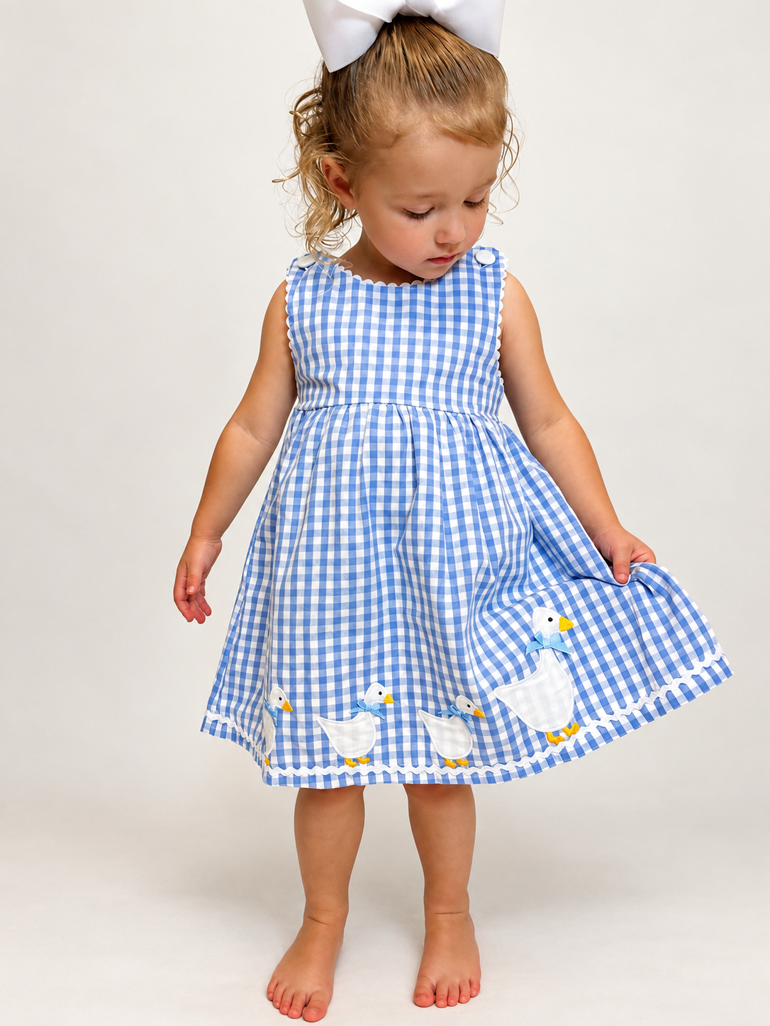 Girl wearing The Little Goose Dress, blue gingham with goose applique hem