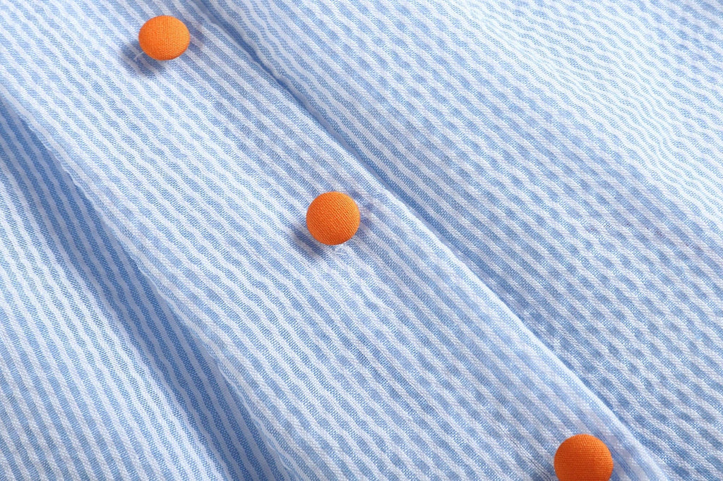 Close-up of blue seersucker fabric and orange buttons
